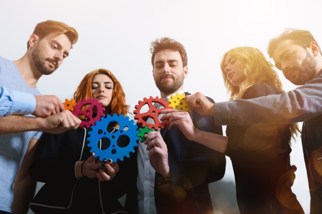 Varias personas sujetando engranajes de colores simulando trabajo en equipo